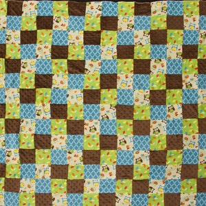May include: A patchwork quilt with a brown, blue, green, and beige color scheme. The quilt is made of squares with different patterns, including owls, leaves, and geometric designs.