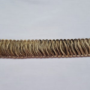 May include: Gold fringe trim with a wavy texture. This trim is perfect for adding a touch of elegance to any project.