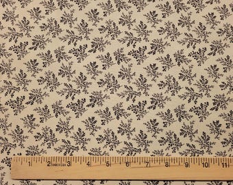 May include: A beige fabric with a repeating pattern of small black fern-like leaves. A wooden ruler is placed at the bottom of the image.
