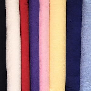May include: A vertical arrangement of fabric rolls in various colors. The colors include black, white, red, purple, pink, yellow, navy blue, and light blue. The fabric has a textured appearance, suggesting a woven or embossed design.