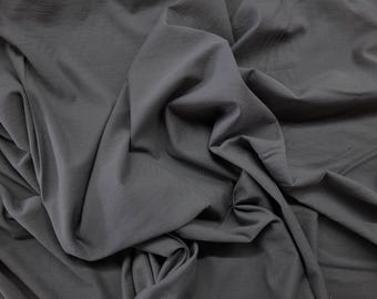 May include: Close-up of a dark gray fabric with soft folds and a subtle sheen. The textile appears to be lightweight and drapes gracefully, suggesting it could be used for clothing or home decor.