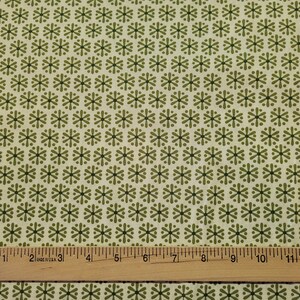 May include: A beige fabric with a repeating pattern of green starbursts. A wooden ruler is placed at the bottom of the image.