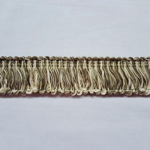 May include: A close-up of a brown and cream fringe trim. The fringe is made of a soft, woven fabric and has a subtle texture.