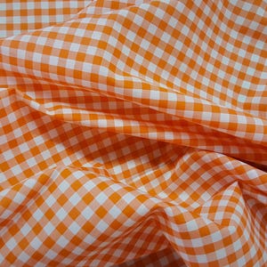 May include: Orange and white gingham fabric with a checkered pattern. The fabric is folded and wrinkled.