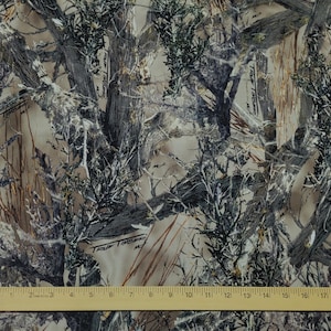May include: Camouflage fabric with a pattern of tree branches and foliage in shades of brown, gray, and green. A wooden ruler with inch markings is at the bottom of the image.