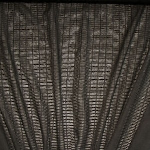 May include: Black sheer fabric with a textured woven pattern. The fabric is slightly wrinkled and has a soft, drapey feel.
