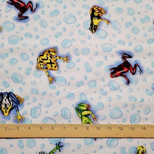 May include: White fabric with a pattern of colorful frogs and blue water droplet shapes. The frogs are in various colors, including red, yellow, green, and blue. A wooden ruler is at the bottom of the image.