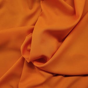May include: A close-up of a smooth, orange fabric with soft folds and wrinkles.