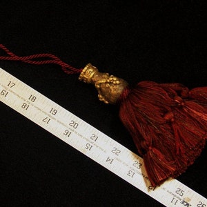 May include: A burgundy tassel with a gold metal top. The tassel is about 3 inches long and has a cord loop for hanging.