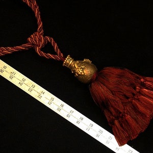May include: A burgundy tassel with a gold metal top. The tassel is approximately 18 inches long and is made of a soft, silky material.