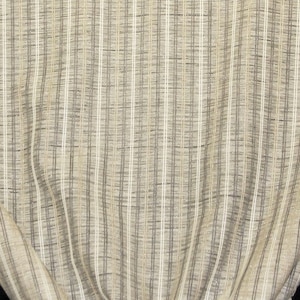 May include: Close-up of a fabric with a woven texture. The fabric features vertical stripes in shades of beige, gray, and white. The material is draped, showing folds and a glimpse of a black background. The overall appearance suggests a textile for home decor or apparel.