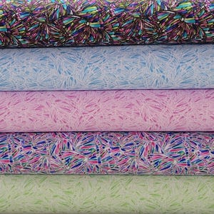 May include: Five rolls of fabric with different patterns. The top roll is black with a colorful geometric pattern. The second roll is light blue with a white geometric pattern. The third roll is pink with a white geometric pattern. The fourth roll is white with a colorful geometric pattern. The bottom roll is light green with a white geometric pattern.