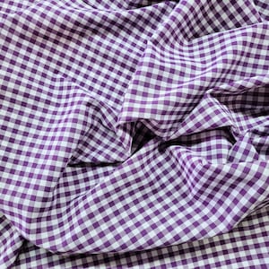 May include: Purple and white gingham fabric with a checkered pattern. The fabric is folded and wrinkled.