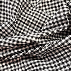 May include: Black and white gingham fabric with a checkered pattern. The fabric is folded and wrinkled, creating a textured look.