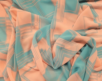 May include: A flowing fabric with a geometric pattern in shades of peach and teal. The design features a repeating pattern of squares and lines, creating a modern and elegant look. The fabric is draped, showing its soft texture and potential for apparel or home decor.