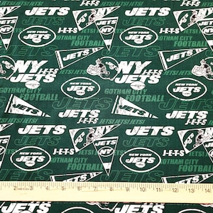 May include: Green fabric with a repeating pattern of the New York Jets logo, team name, and "J-E-T-S" text. The fabric also includes a ruler for scale.