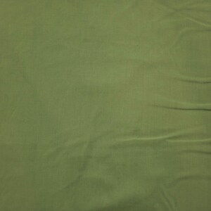 May include: Close-up of olive green fabric with visible texture and folds. The material has a slightly wrinkled appearance, suggesting it is soft and pliable. The color is a muted, earthy tone.