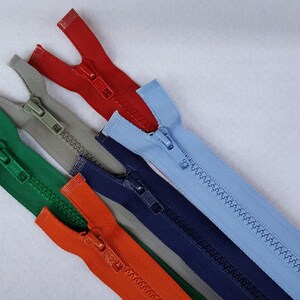 May include: Five different colored zippers, including green, orange, red, blue, and gray. The zippers are laid out in a fan shape on a white surface.