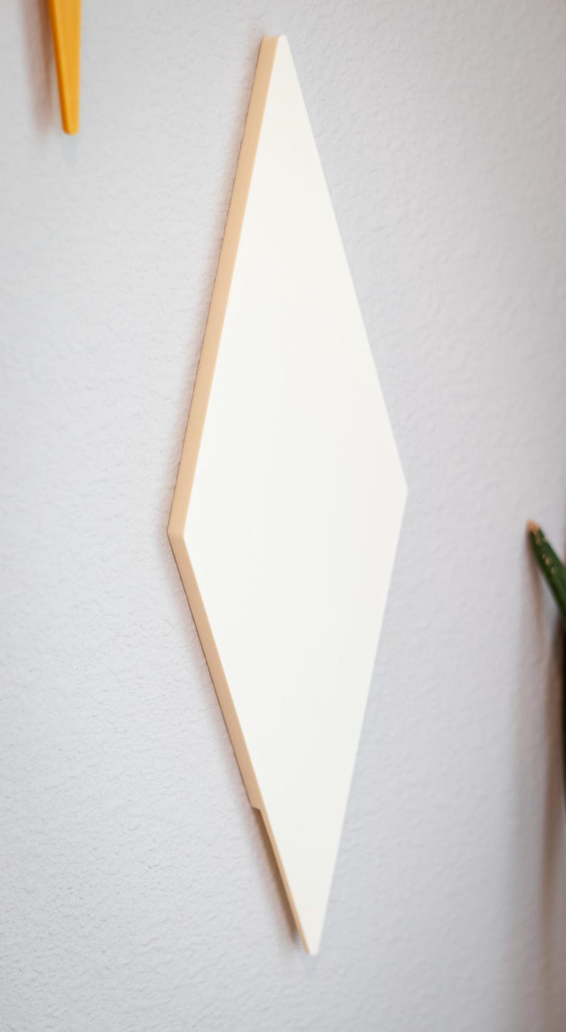Puede incluir: Decoraci&oacute;n de pared en forma de rombo de color crema. La pieza de arte geom&eacute;trico est&aacute; montada en una pared gris claro. El rombo tiene un borde biselado y est&aacute; ligeramente inclinado hacia el espectador.