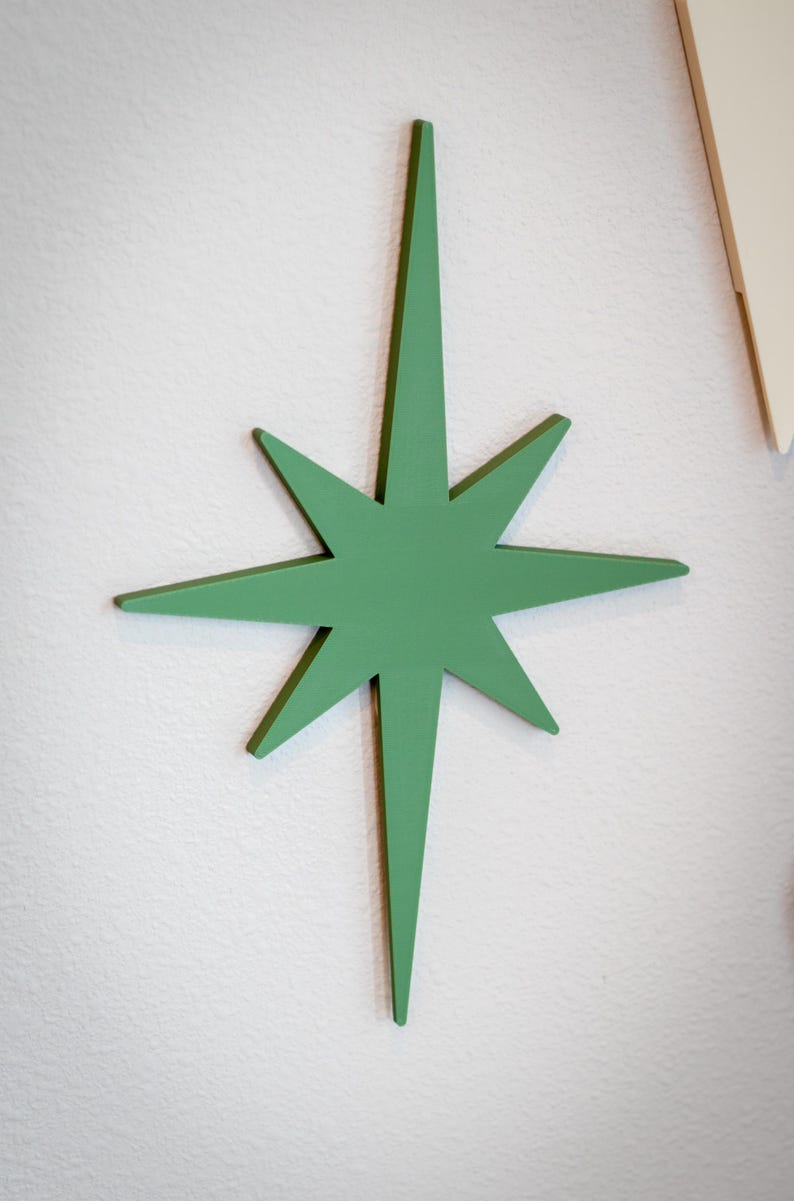 Puede incluir: Decoraci&oacute;n de pared en forma de estrella verde de ocho puntas. La estrella est&aacute; pintada de verde liso y est&aacute; montada en una pared blanca. Esta pieza decorativa a&ntilde;ade un toque moderno de mediados de siglo.