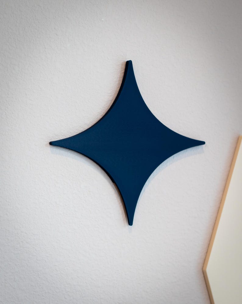 Puede incluir: Decoraci&oacute;n de pared en forma de estrella de cuatro puntas, de color azul marino. La estrella est&aacute; montada en una pared blanca con superficie texturizada. El dise&ntilde;o de la estrella es simple y moderno, adecuado para varios estilos de interior.