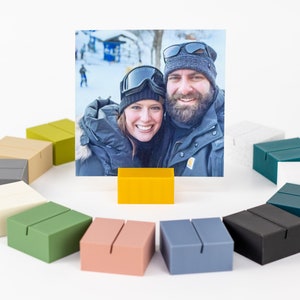 May include: A set of ten photo holders in various colors, including gray, white, beige, green, yellow, pink, blue, and black. The holders are made of a sturdy material and have a slot for holding a photo.