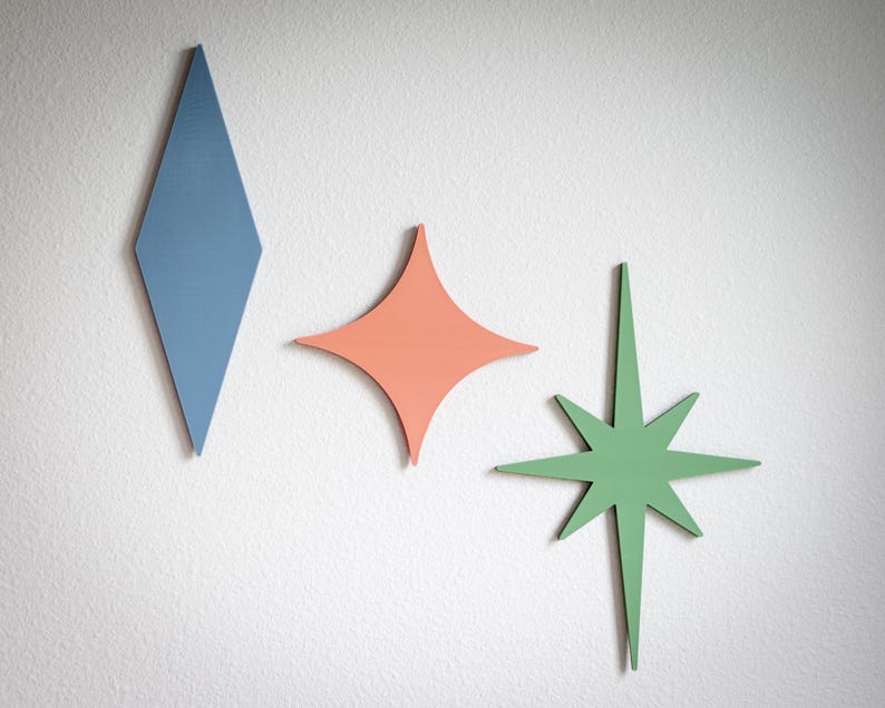 Puede incluir: Tres piezas de decoraci&oacute;n de pared de madera con formas geom&eacute;tricas. Un rombo azul, una estrella de coral y una estrella verde est&aacute;n montadas en una pared blanca. Estas decoraciones de estilo moderno de mediados de siglo a&ntilde;aden un toque de color y un toque retro.