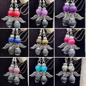 May include: A set of nine pairs of dangle earrings featuring a variety of gemstone colours, including purple, blue, red, green, and brown. Each earring has a silver angel wing charm and a black lava rock bead.