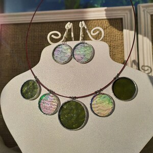 May include: A set of iridescent green and purple glass jewelry with a necklace and earrings. The necklace has five round pendants, two green and three iridescent. The earrings are round and iridescent.