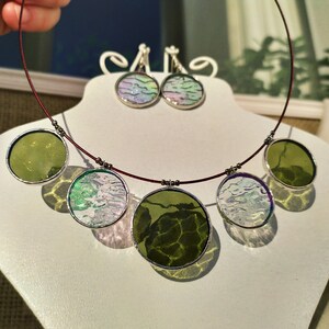 May include: A necklace with five round pendants, two green and three with a white and green marbled design. The necklace is made with a dark red cord and silver metal accents. Matching earrings with a white and green marbled design are also included.