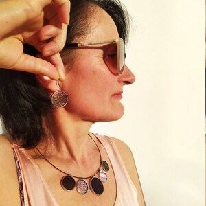 May include: A woman wearing sunglasses and a pink tank top with a necklace featuring multiple round, colorful pendants. She is also wearing a pair of round earrings with a similar design to the necklace pendants.