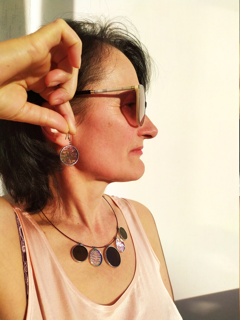 May include: A woman wearing sunglasses and a pink tank top with a necklace featuring multiple round, colorful pendants. She is also wearing a pair of round earrings with a similar design to the necklace pendants.