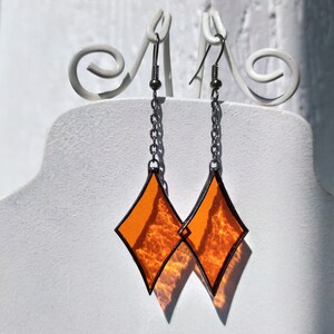 Op de afbeelding: Een paar oranje, diamantvormige glazen oorbellen met zilveren kettingen en haakjes.