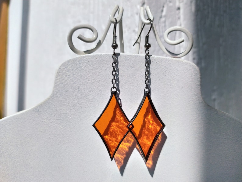 Op de afbeelding: Een paar oranje, diamantvormige glazen oorbellen met zilveren kettingen en haakjes.