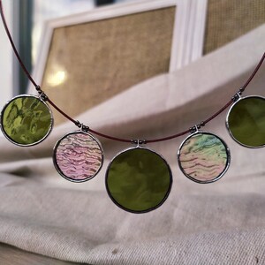 May include: A necklace with five round glass pendants. The pendants are in shades of green, pink, and white. The necklace is made of a thin red cord.