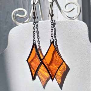 Op de afbeelding: Een paar oranje glazen diamant oorbellen met zilveren kettingen en haken.