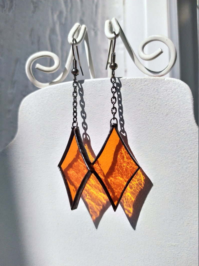 Op de afbeelding: Een paar oranje glazen diamant oorbellen met zilveren kettingen en haken.