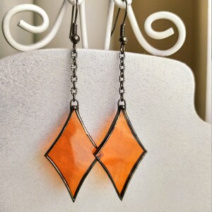 Op de afbeelding: Een paar oranje diamantvormige oorbellen met een zilveren ketting en een haaksluiting.