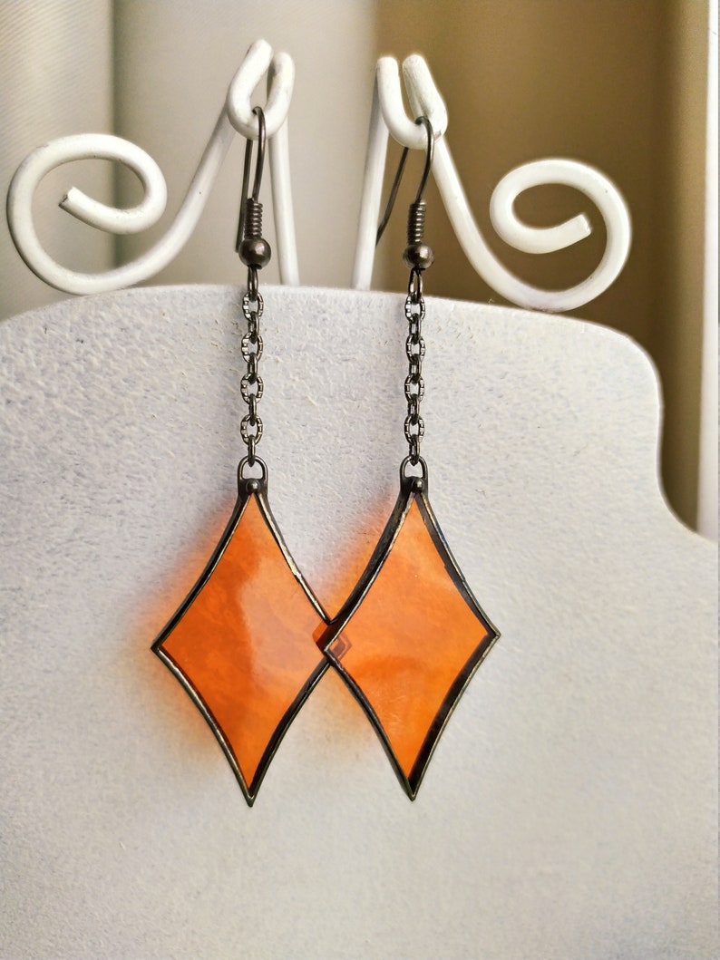 Op de afbeelding: Een paar oranje diamantvormige oorbellen met een zilveren ketting en een haaksluiting.