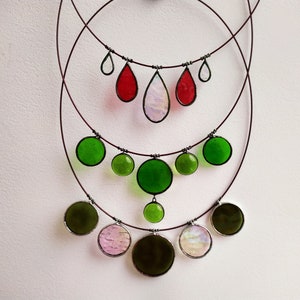 May include: A multi-layered necklace with green, red, and iridescent glass teardrop and round pendant charms. The necklace is made of wire and has a delicate, feminine look.