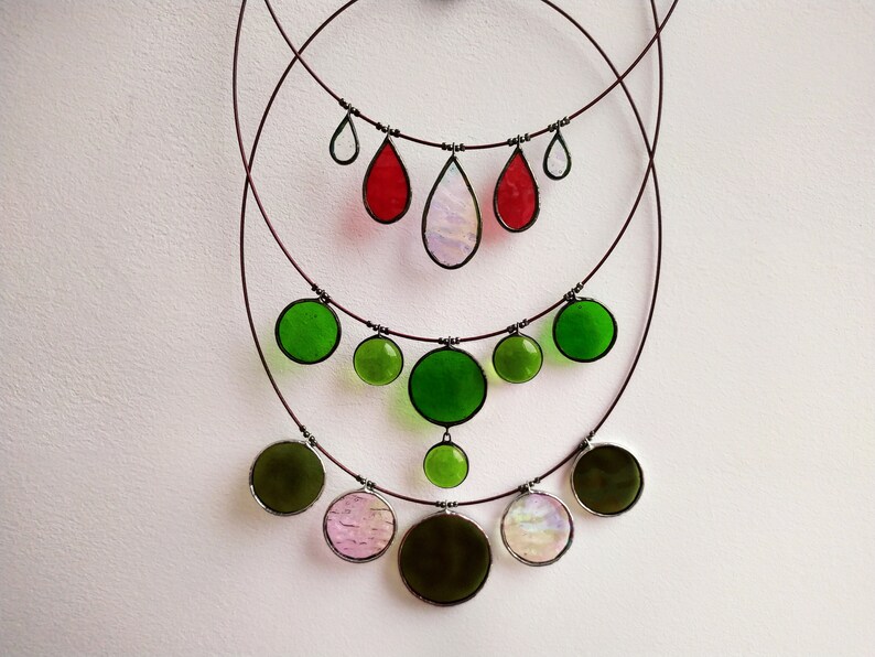 May include: A multi-layered necklace with green, red, and iridescent glass teardrop and round pendant charms. The necklace is made of wire and has a delicate, feminine look.