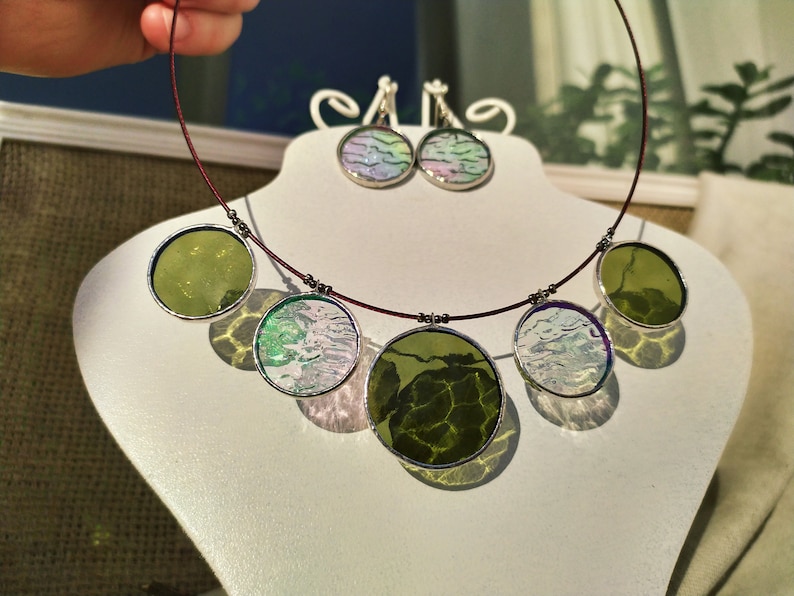 May include: A necklace with five round pendants, two green and three with a white and green marbled design. The necklace is made with a dark red cord and silver metal accents. Matching earrings with a white and green marbled design are also included.