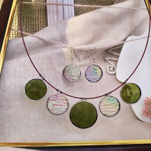 May include: A red cord necklace with five round pendants. The pendants are made of glass and feature different patterns, including green, pink, and white.