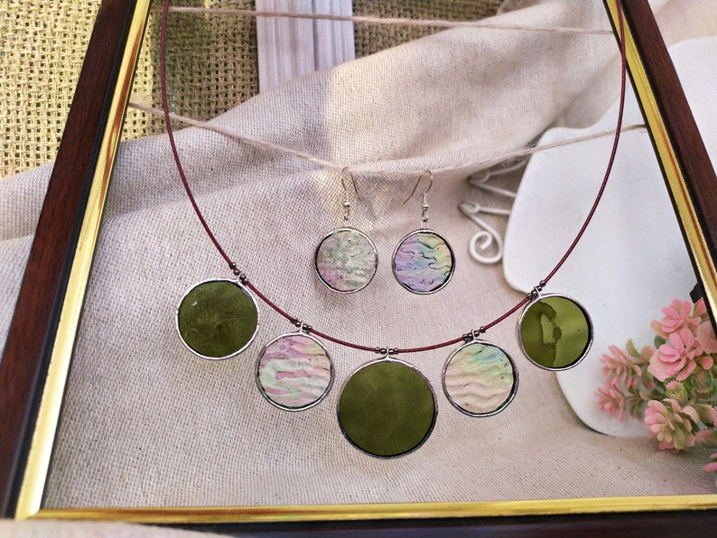 May include: A red cord necklace with five round pendants. The pendants are made of glass and feature different patterns, including green, pink, and white.