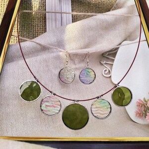 May include: A set of green and iridescent glass circle earrings and necklace. The necklace has five circles, two green and three iridescent. The earrings are both iridescent.