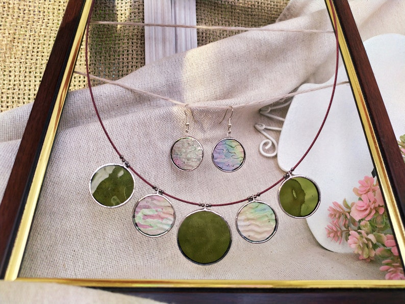 May include: A set of green and iridescent glass circle earrings and necklace. The necklace has five circles, two green and three iridescent. The earrings are both iridescent.