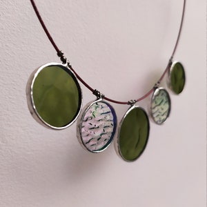 May include: A necklace with five round glass pendants. The pendants are in shades of green and white with a silver trim. The necklace is made of a thin red cord.