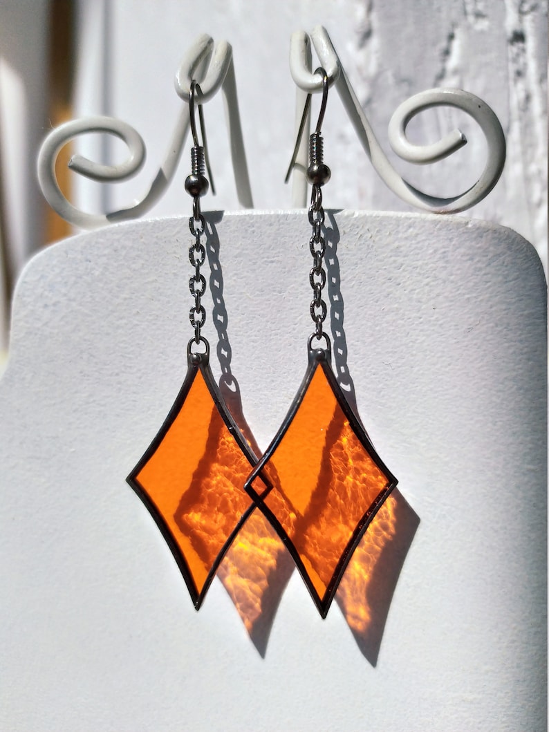 Op de afbeelding: Een paar oranje ruitvormige glas-in-lood oorbellen met zilveren kettingen en haken.