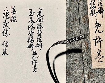 May include: Close-up of a scroll with Japanese calligraphy. The scroll is tied with a black ribbon and has a textured fabric covering. The text on the scroll reads "九存"