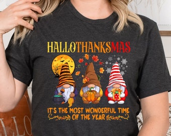 Könnte beinhalten: Dunkelgraues Heather-T-Shirt mit dem Text "HALLOTHANKSMAS" und drei festlichen Zwergen. Die Zwerge sind in Halloween-, Thanksgiving- und Weihnachtskleidung gekleidet. Der Text "IT'S THE MOST WONDERFUL TIME OF THE YEAR" ist ebenfalls auf dem Shirt.